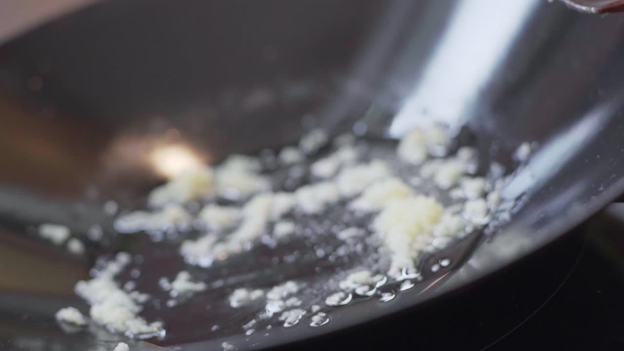 Close up of sliced garlic with oil sizzling in a black wok pot