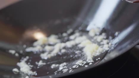 close up of sliced garlic with oil sizzling in a black wok pot