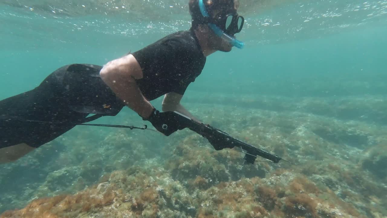 Side shot of spearfisher snorkeling in the mediterranean sea in very shallow waters looking for fish
