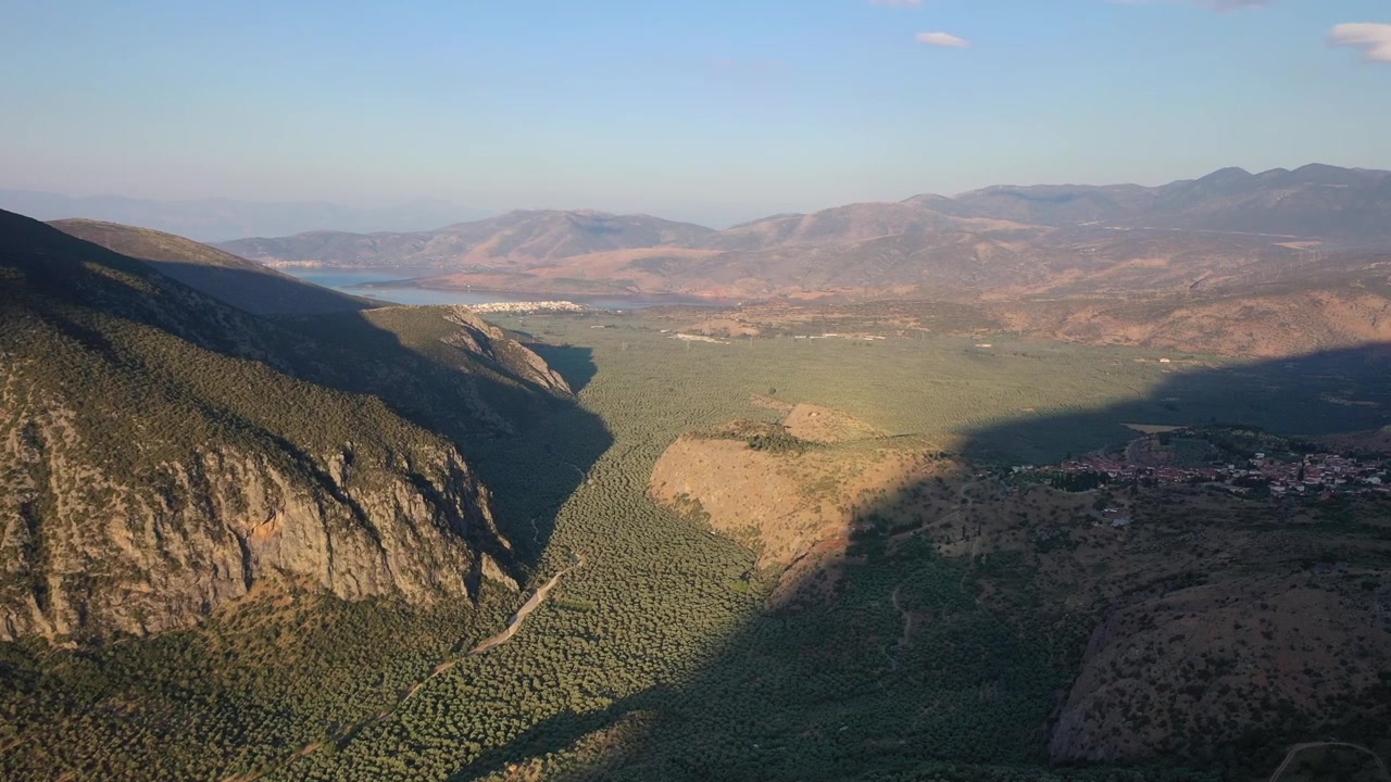 Splendida ripresa con drone di una strada serpeggiante che attraversa il fianco verde e roccioso della montagna di Delfi. Il filmato mostra il vasto e selvaggio paesaggio del Monte Parnaso sotto un cielo luminoso e nuvoloso