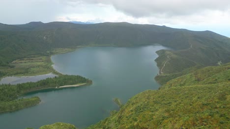vista aérea panorámica de la lagoa do fogo rodeada de exuberantes colinas verdes bajo un cielo nublado
