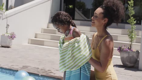 madre y hija afroamericanas felices secándose con una toalla junto a la piscina, cámara lenta