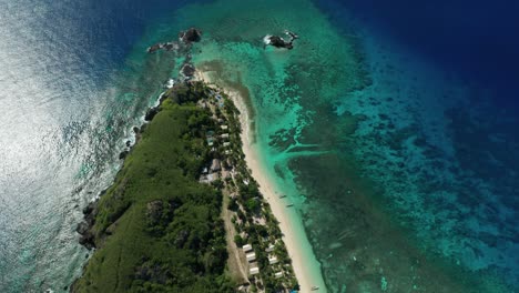 fiji islands - coral reef under the clear blue ocean water surrounding the pristine tropical island in fiji with green trees and white sand - aerial shot