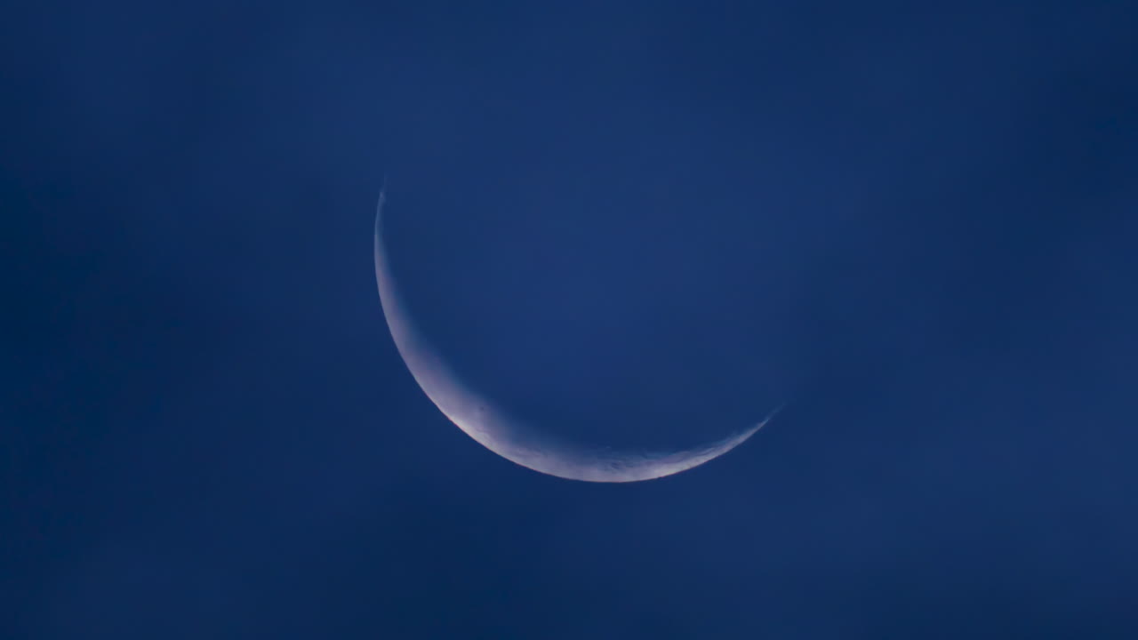 Close up of a thin crescent moon glowing against a deep blue night sky