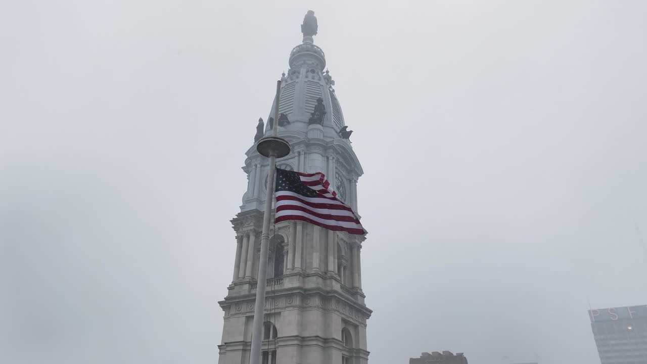 Vista aérea da prefeitura da Filadélfia com a icônica torre do relógio enquanto uma grande bandeira americana tremula fortemente ao vento no inverno sob um céu nublado. Orgulho cívico patriótico no centro da Filadélfia, EUA