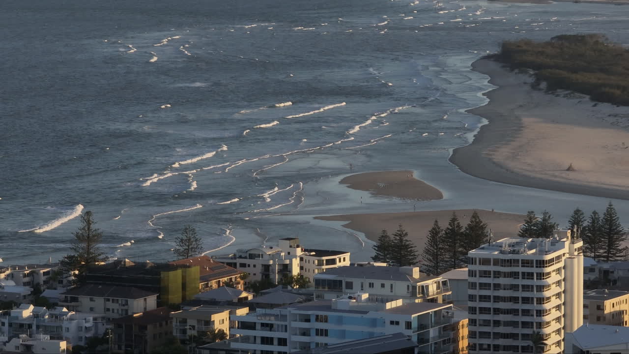 Drone costiero sopra appartamenti fronte mare che si affacciano su onde blu dell'oceano in una città costiera australiana, 4K, teleobiettivo, parallasse