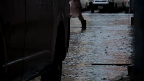 man walking through the flooded street with knee high boots in a city with submerged cars parked nearby in al nahda, sharjah, united arab emirates after a heavy rain on november 26, 2018