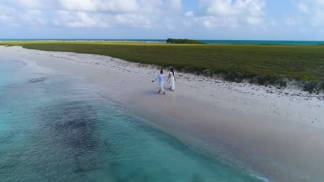 pareja caminando con ropa blanca y descalza en la playa caribeña de arena blanca en los roques