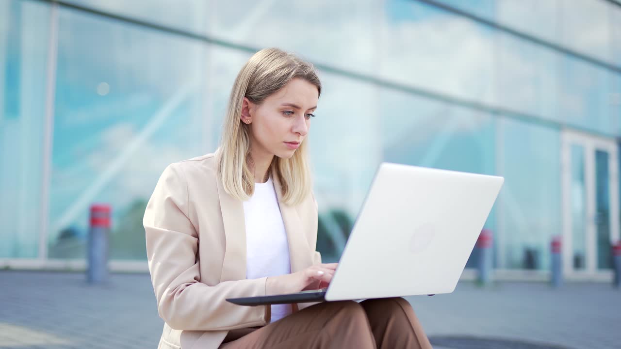 보행자길에 앉아 노트북으로 일하는 젊은 사업가 여성, 현대 사무실 센터의 도시 배경.