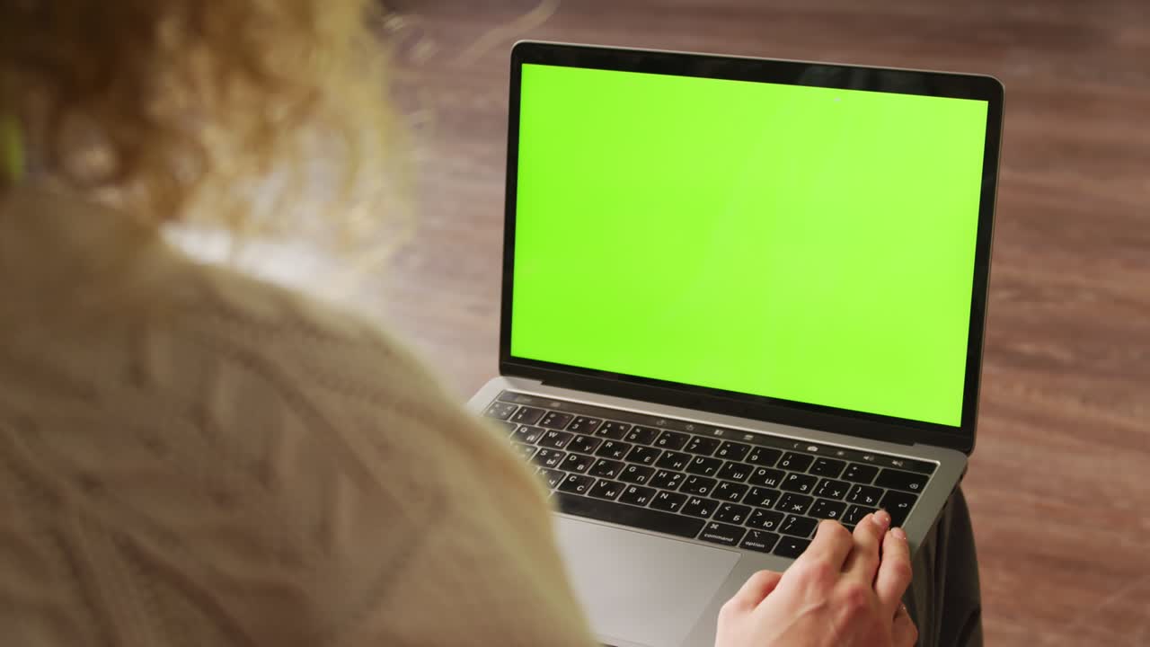 cámara lenta de mano sobre el hombro de una mujer rizada sosteniendo una computadora portátil con una llave de croma de pantalla verde en sus rodillas