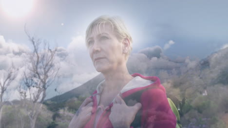 feliz caucásica mujer mayor caminando en las montañas sobre nubes de rápido movimiento