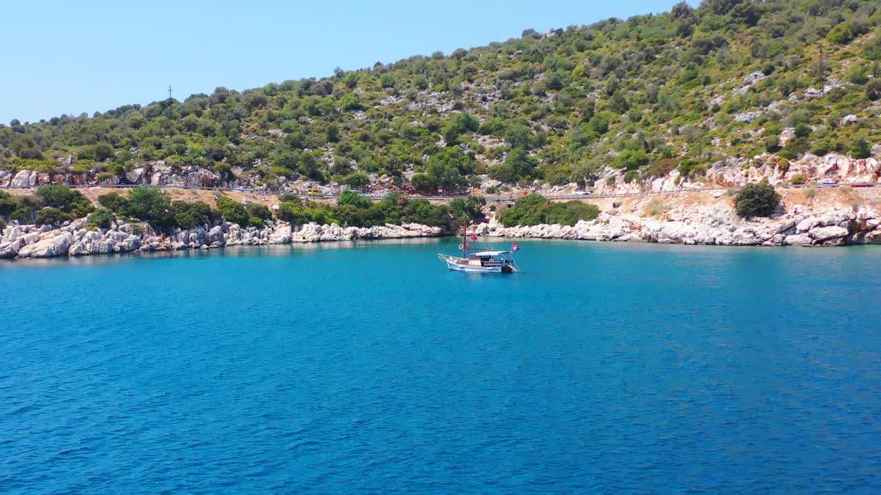 Aerial drone flying towards a sailboat anchored in the tropical blue Mediterranean Sea alongside a rocky beach near Finike Turkey
