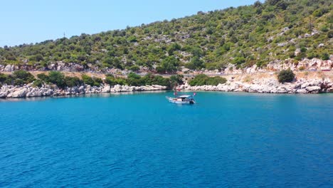 aerial drone flying towards a sailboat anchored in the tropical blue mediterranean sea alongside a rocky beach near finike turkey