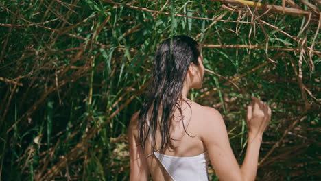 brunette touching wet hair at sunshine jungles back view. woman looking camera