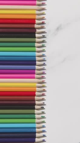 video vertical de lápices de colores dispuestos en una línea sobre un fondo de mármol blanco