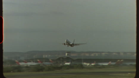 filmed on super 8 film vintage footage shows an airplane taking off from a runway, with other planes visible in the background and a control tower