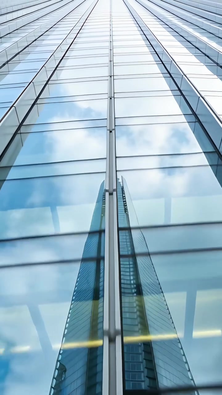 Vídeo vertical: Câmera inclinando mostrando parede de vidro refletindo torre no centro da cidade, centralizando o reflexo.