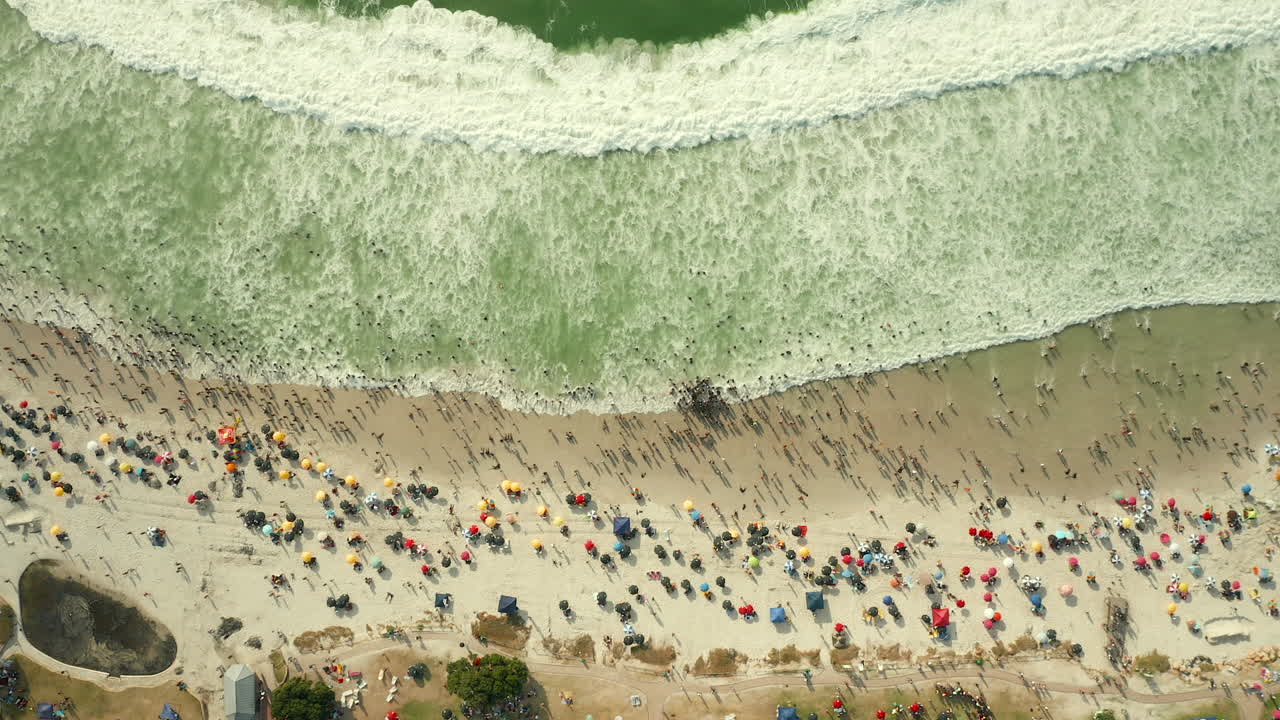 vista aérea de turistas en la playa de camps bay con sombrillas de playa en verano en ciudad del cabo, sudáfrica