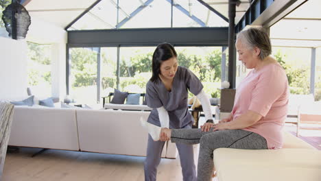 physiotherapist assisting senior asian woman with leg exercises in home setting