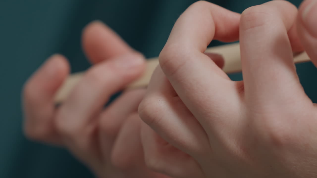 Expert practitioner performing detailed nail shaping process. Close view of professional meticulously shaping nails using beige file against teal background demonstrating expert hand care techniques