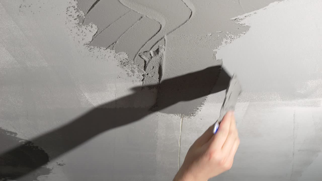 A man is applying decorative plaster to a gray wall from above