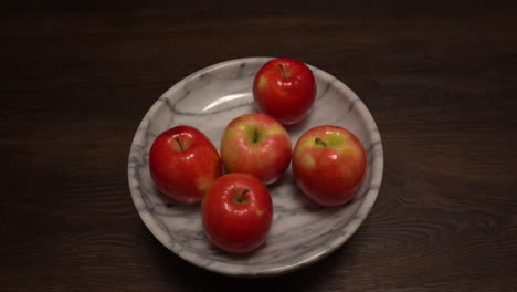 closeup of woman adding red apples to a white marble bowl