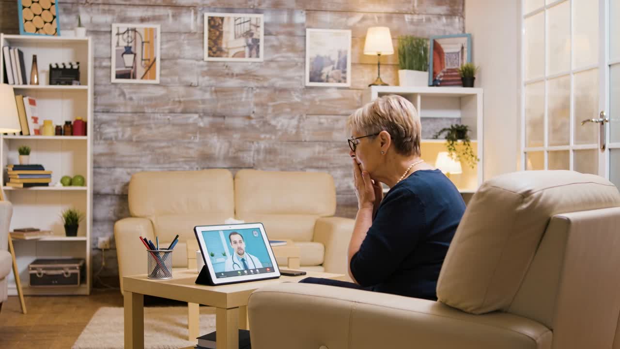 Doctor calling, senior woman in navy top listening, touching mouth for advice on tablet, copy space