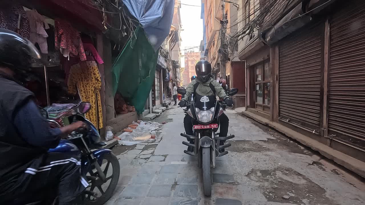 Backseat view of a car navigating the lively alleys of central Kathmandu, following motorbikers in a dynamic urban commute. Thamel area full of stores and narrow alleys