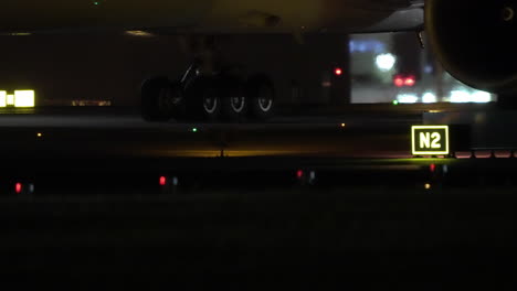 closeup of airplane landing gear on illuminated taxiway at night with green red and yellow lights