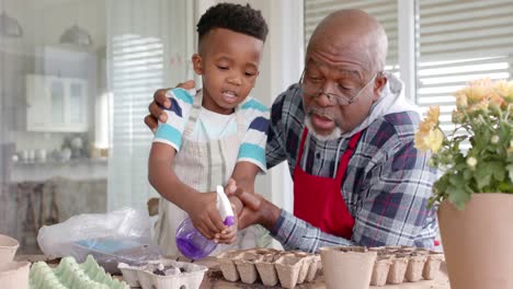 Happy-african-american-grandfather-and-grandson-embracing,-planting-flowers-on-balcony,-slow-motion