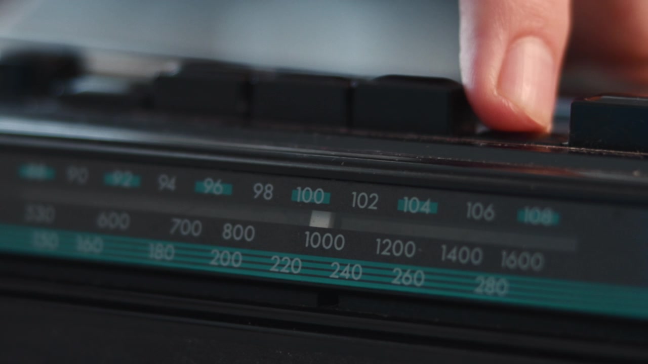 Vista ravvicinata del pannello di un sintonizzatore radio vintage con una manopola centrale, marcature di frequenza numerate e manopole di controllo scure in una luce interna soffusa