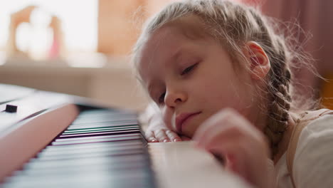 sleepy little girl lies and strokes piano keys at home