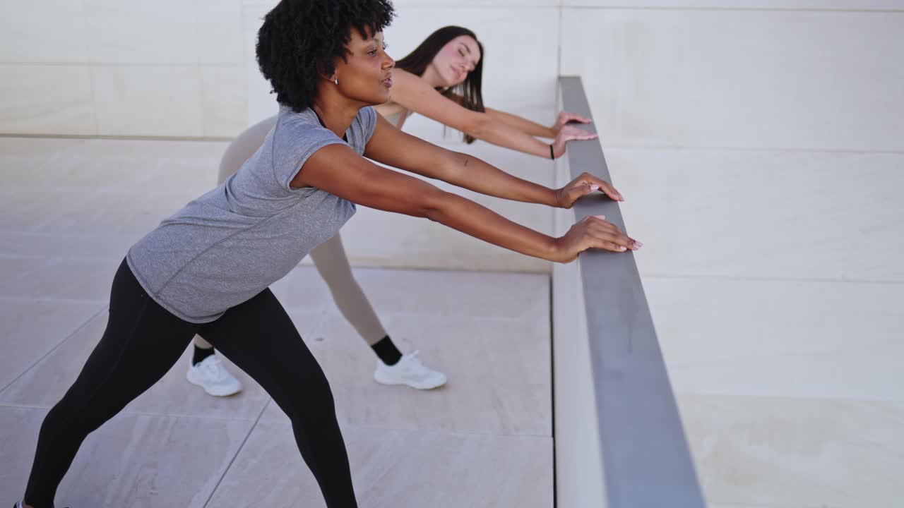 Two Young Women Stretching Outdoors Against a Railing