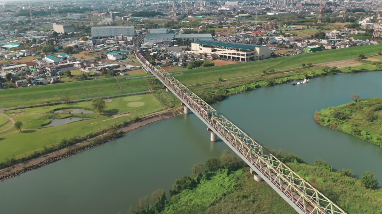 volando sobre el río arakawa con trenes que pasan por el puente ferroviario que domina la ciudad de fujimi en saitama, japón