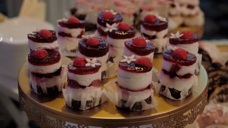 Close-up-shot-with-a-gold-cake-stand-filled-with-multiple-cupcakes-with-strawberries,-tracking-shot