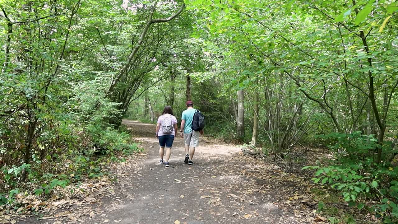 Couple walking on the path in the forest and exploring nature. Man and woman with backpacks hiking in woods