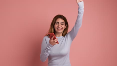 surprised young redhead lady using mobile phone in pink background