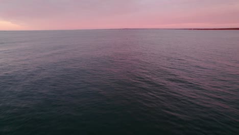 Aerial-of-the-ocean-during-a-pink-sunrise-with-a-kayaker-and-seabirds