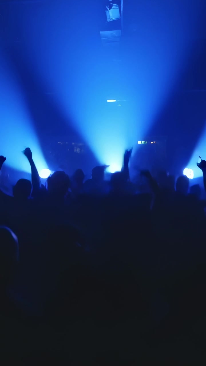 Video verticale: Luci di scena pulsanti che animano una folla scura che alza le mani in un club, con foschia e telefoni