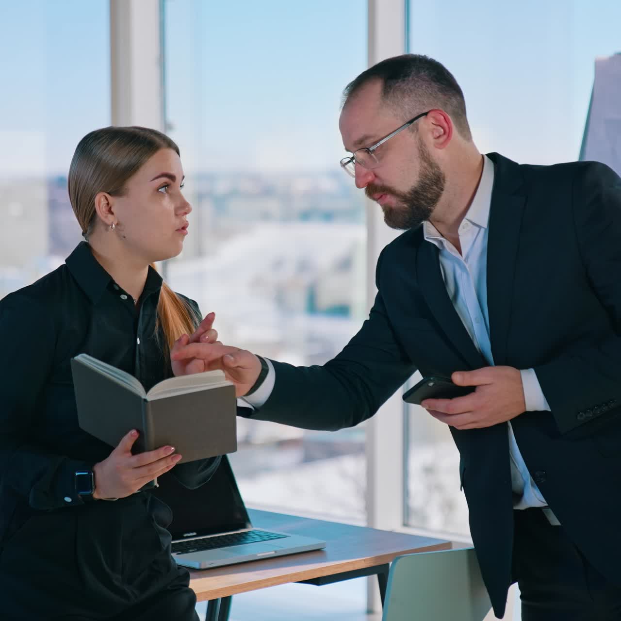 Business colleagues in the light office. Entrepreneur in black suit talking with his female secretary. Large window with city background
