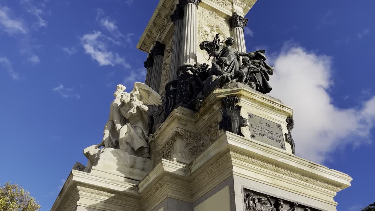 Monument to Alfonso XII in El Retiro Park, Madrid, Spain. Grand neoclassical stone monument with bronze statues overlooking the Retiro pond under bright blue skies