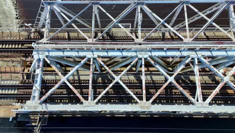 Aerial-view-of-a-red-blue-railroad-bridge-spanning-a-wide,-winding-river-surrounded-by-green-forests-in-a-sunny-day