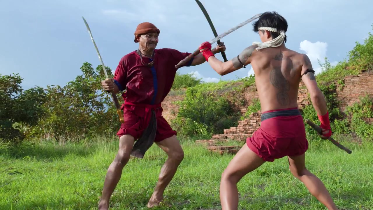 Due antichi guerrieri thailandesi che si allenano con doppie spade su un campo erboso ad Ayutthaya