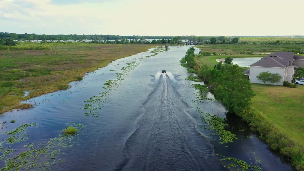 Riprese con drone che seguono una barca che naviga lungo il tortuoso fiume Palatlakaha a Clermont, Florida, incorniciato da rigogliose zone umide e il lago Minneola in lontananza