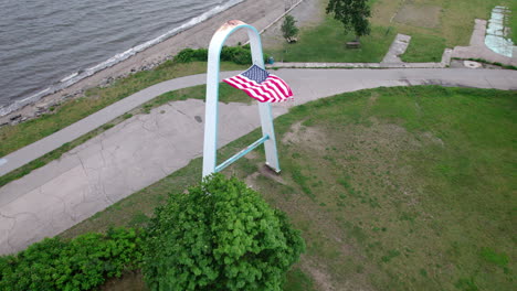 Aerial-video-passing-over-arch-with-American-Flag-in-the-wind,-Rocky-Point,-RI