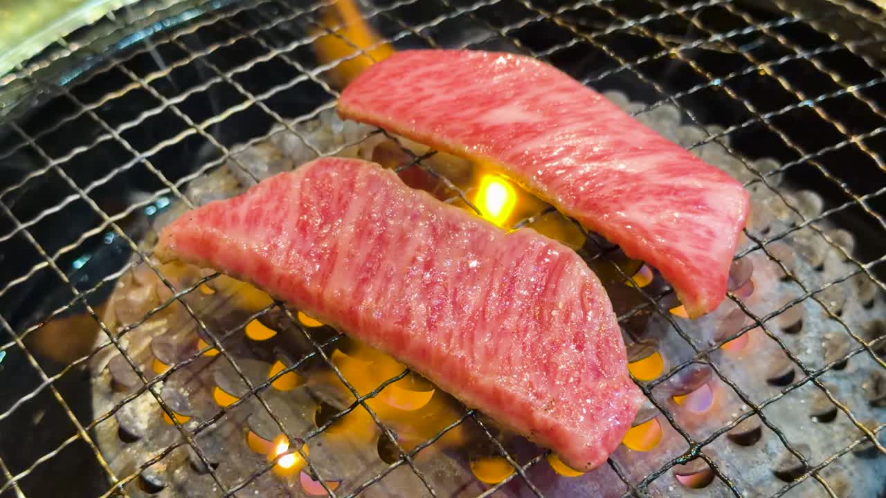 Primo piano di carne di manzo cruda marmorizzata che cuoce su una griglia a carbone con fiamme arancioni tremolanti.