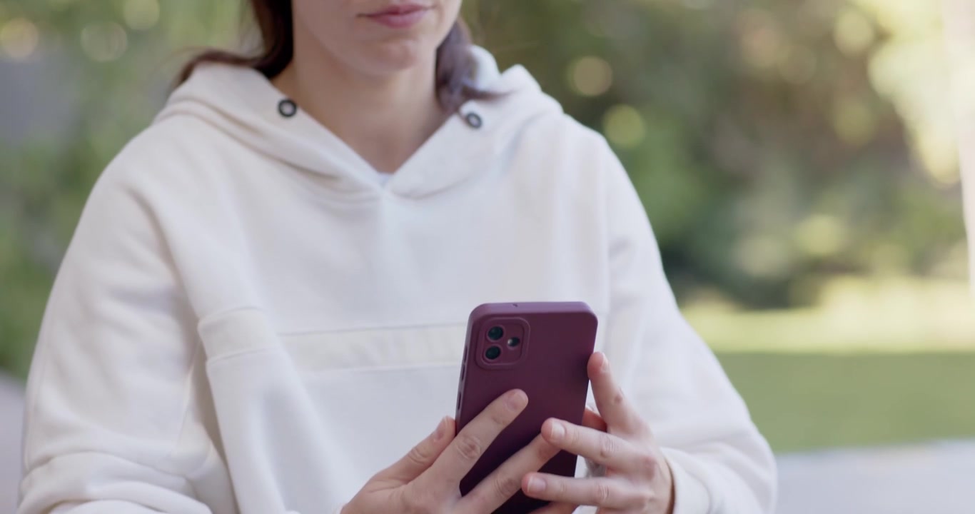 Donna asiatica che vede un cellulare bordeaux su un tappetino verde, si allunga per prenderlo, lo solleva, indossa le cuffie e ascolta sul ponte.