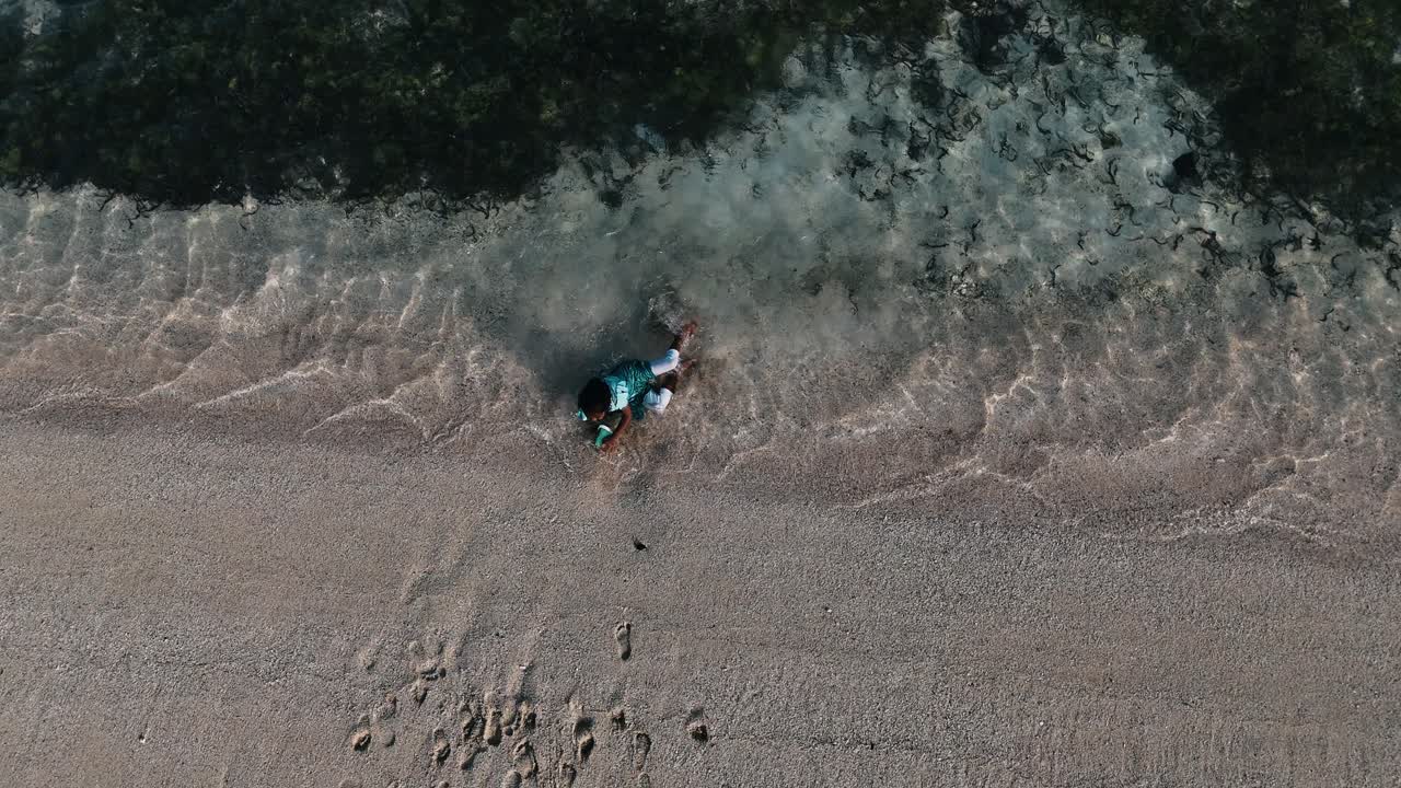 Top-down aerial view of a small girl joyfully playing in the crystal clear, shallow water of a Mauritius beach. Concept of childhood innocence, tropical bliss, and pure water play
