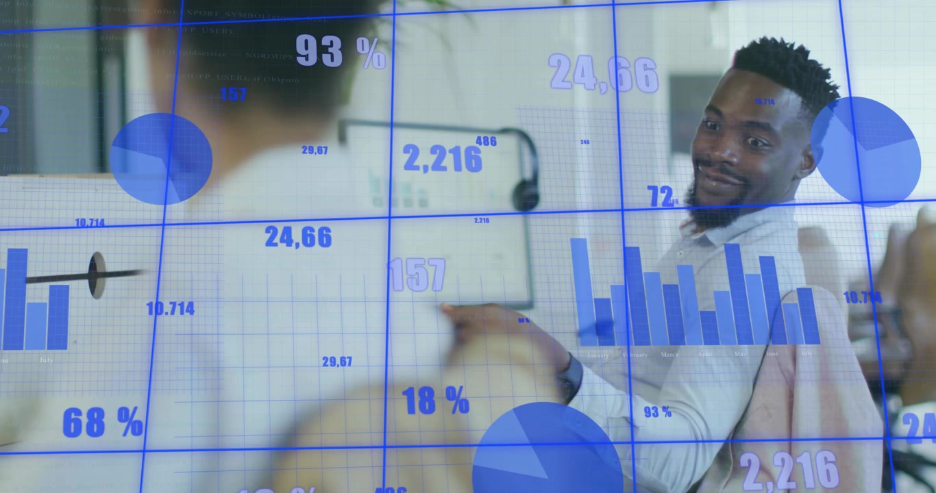 Business analyst monitoring data, charts rising to 94%, colleague passing red notebook for review