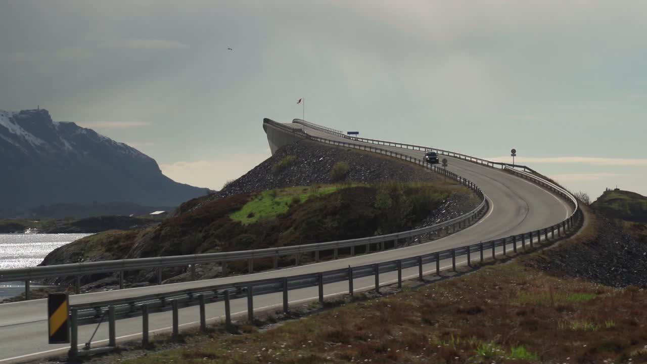 A view of the famous Atlantic Road in Norway. One of its'  arched bridges rises above the sea. It is overcast, with heavy clouds hanging above the water.
